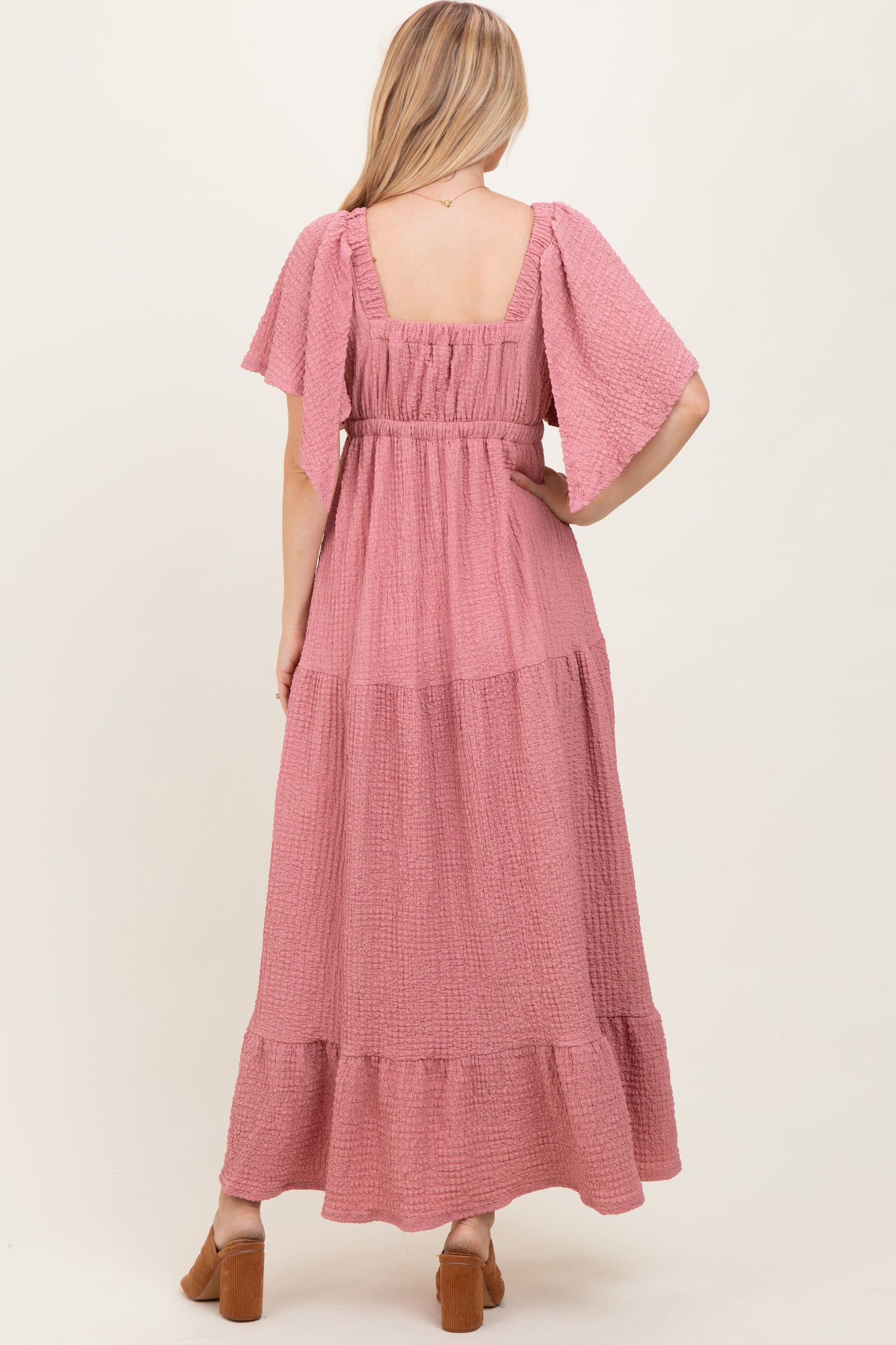 woman wearing a dusty rose maxi dress with flutter sleeves and a tiered skirt, seen from the back