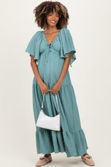 woman wearing a teal maternity maxi dress with flutter sleeves and a baby bump, holding a white handbag