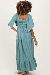 woman wearing a teal maternity maxi dress with flutter sleeves and tiered ruffle hem