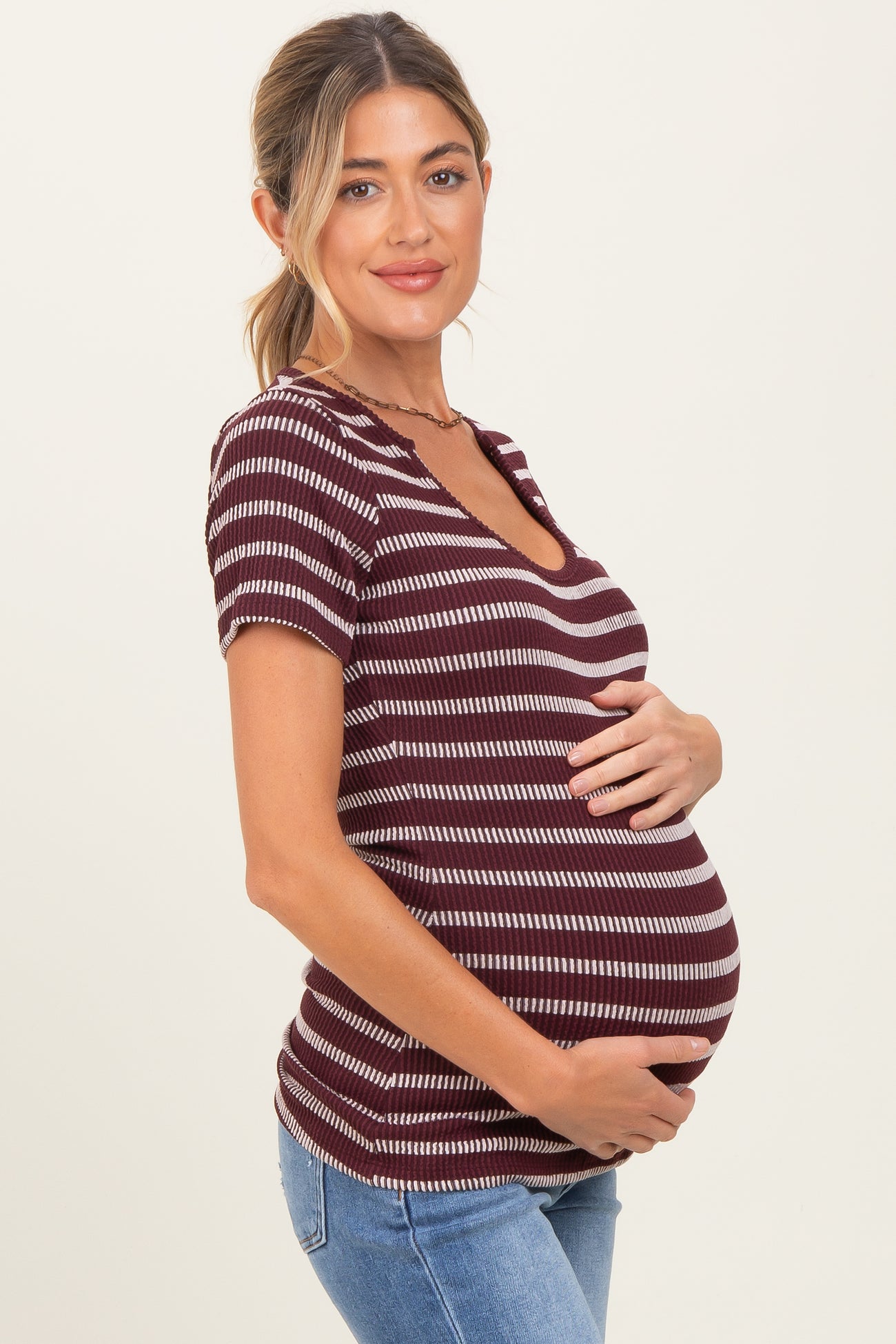 woman wearing a burgundy and white striped maternity top and holding her baby bump