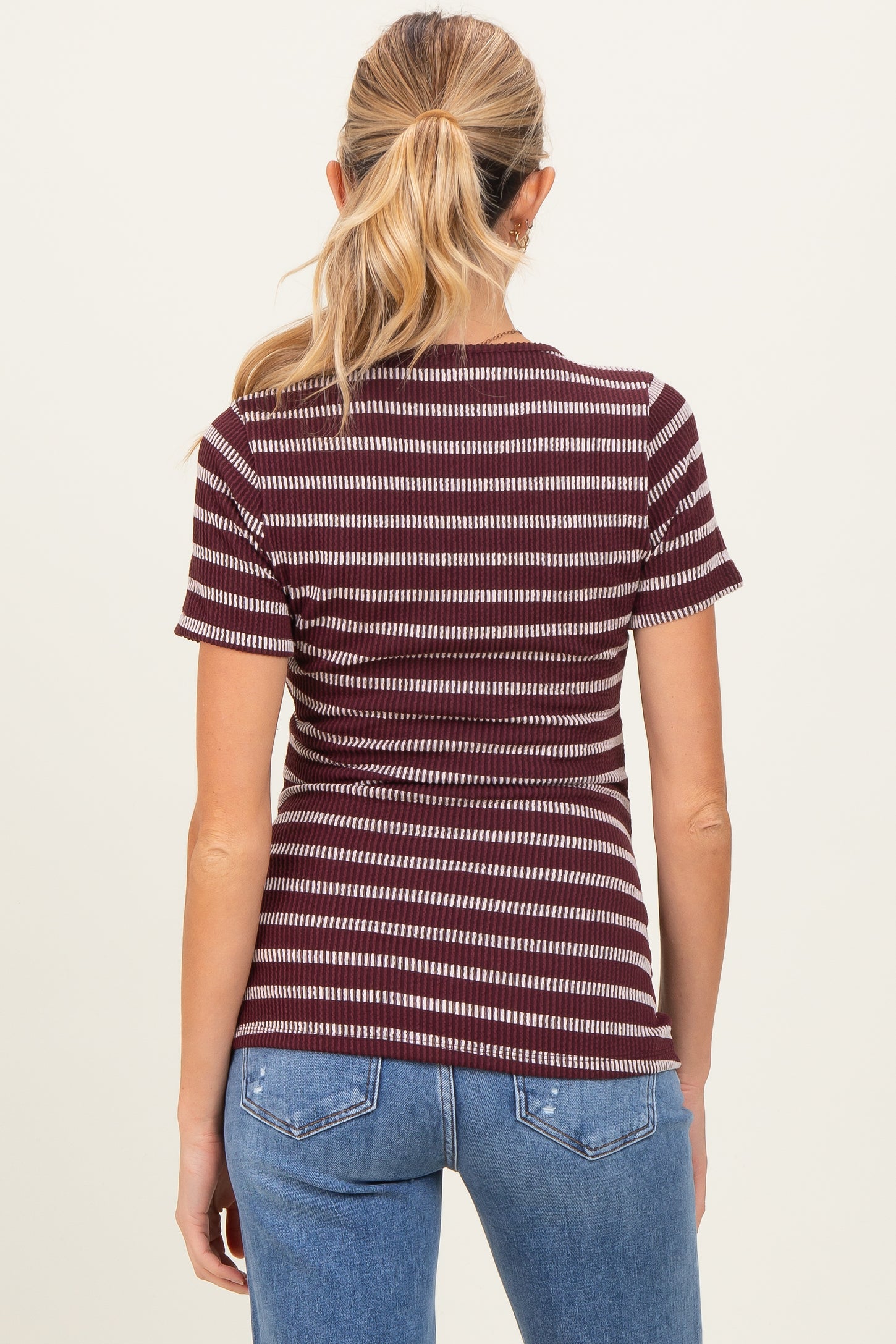 woman wearing a maroon and cream striped maternity top, viewed from the back, paired with blue jeans