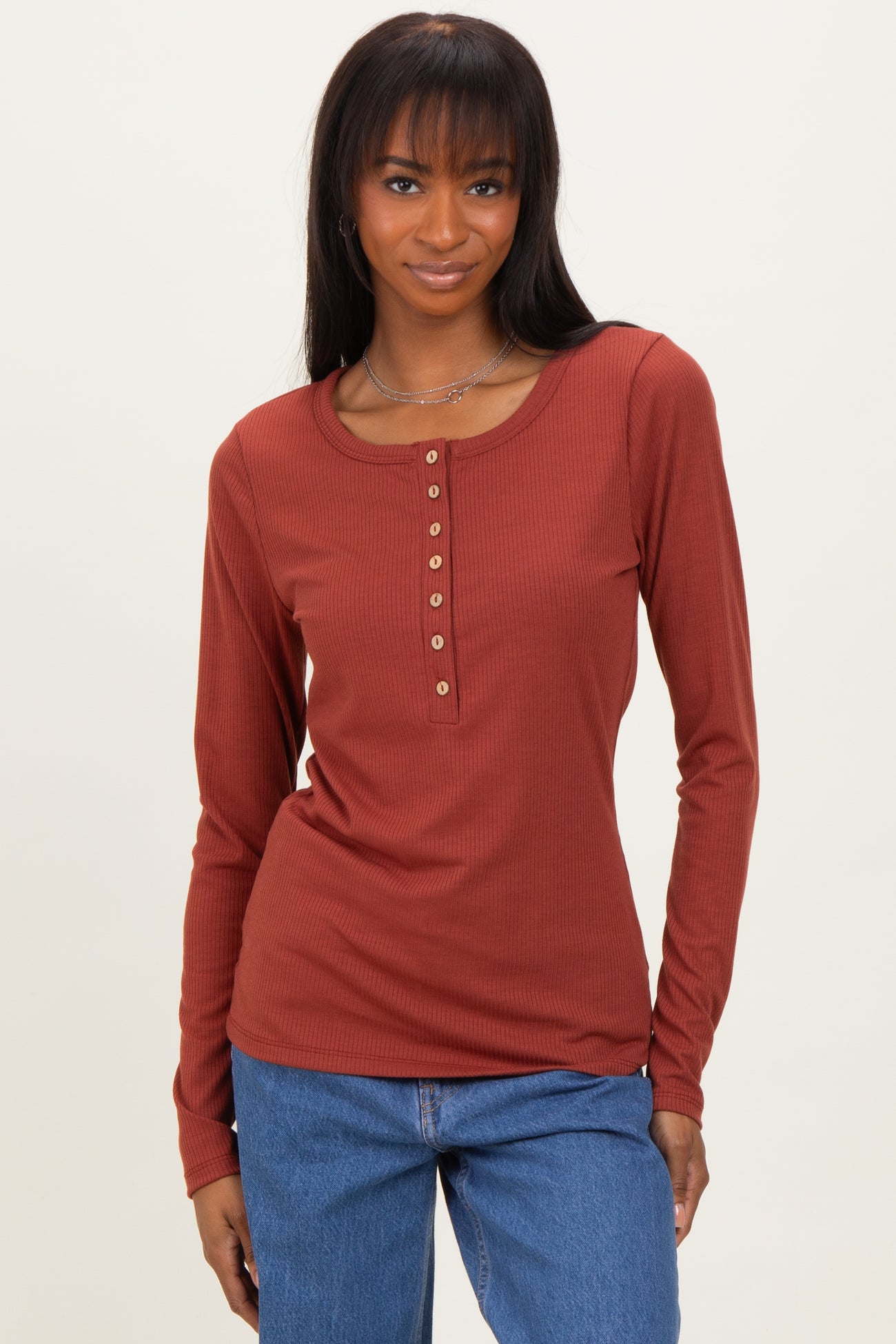 woman wearing a rust long sleeve henley top with button details and light blue jeans