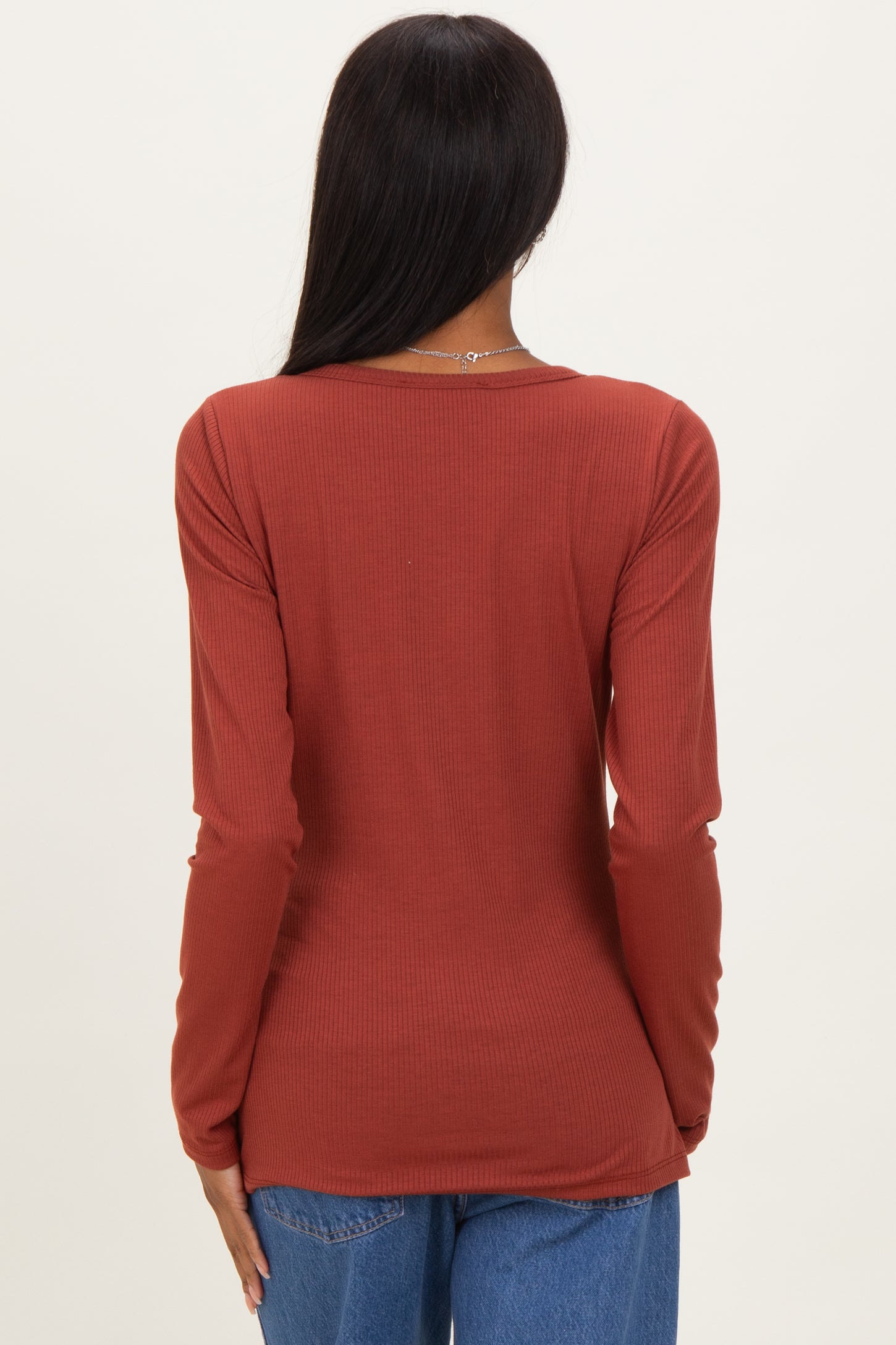 woman wearing a rust-colored long sleeve ribbed top, showing the back view with fitted style and round neckline