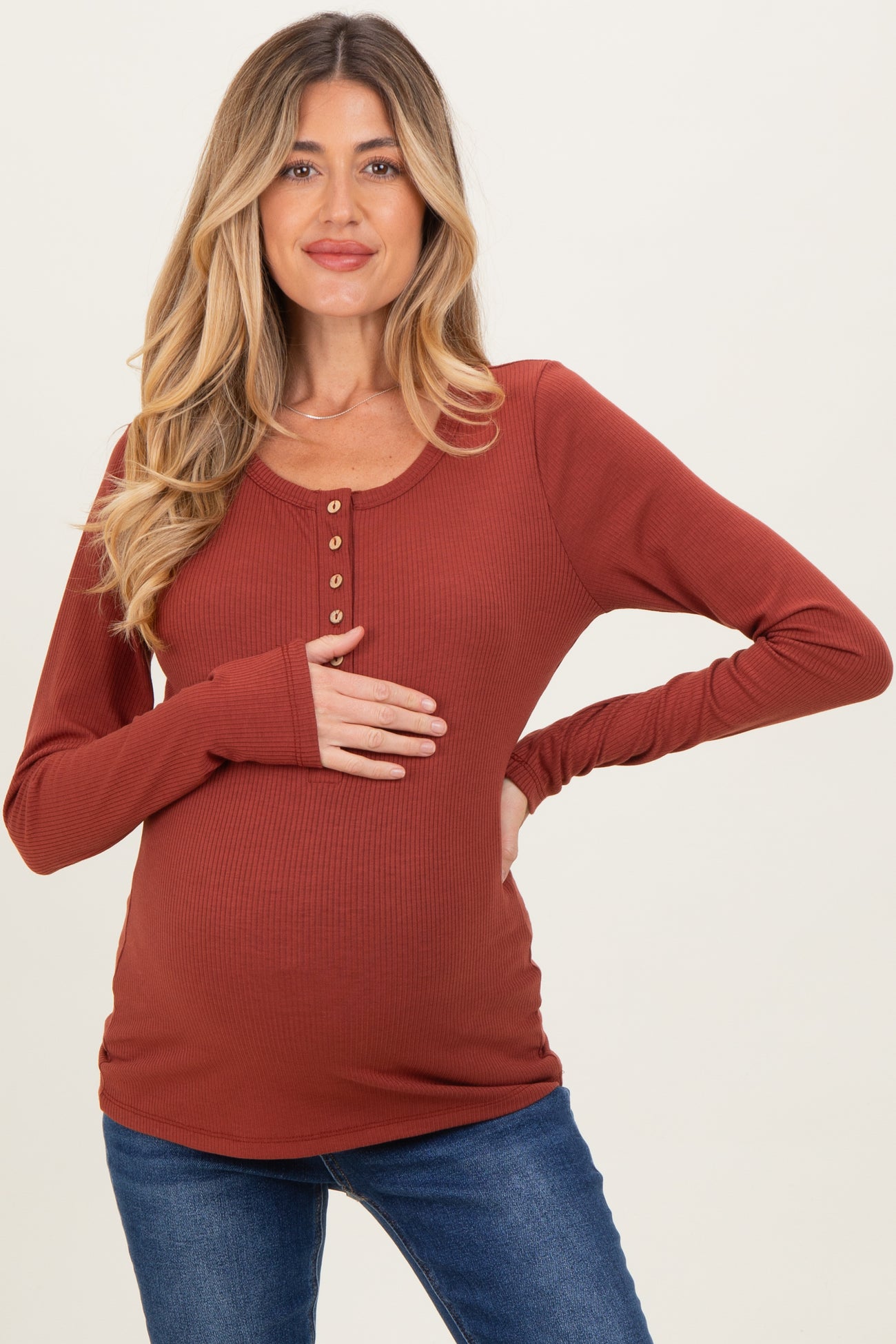 woman wearing a rust colored long sleeve maternity top with button details and holding her baby bump