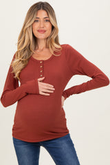 woman wearing a rust colored long sleeve maternity top with button details and holding her baby bump