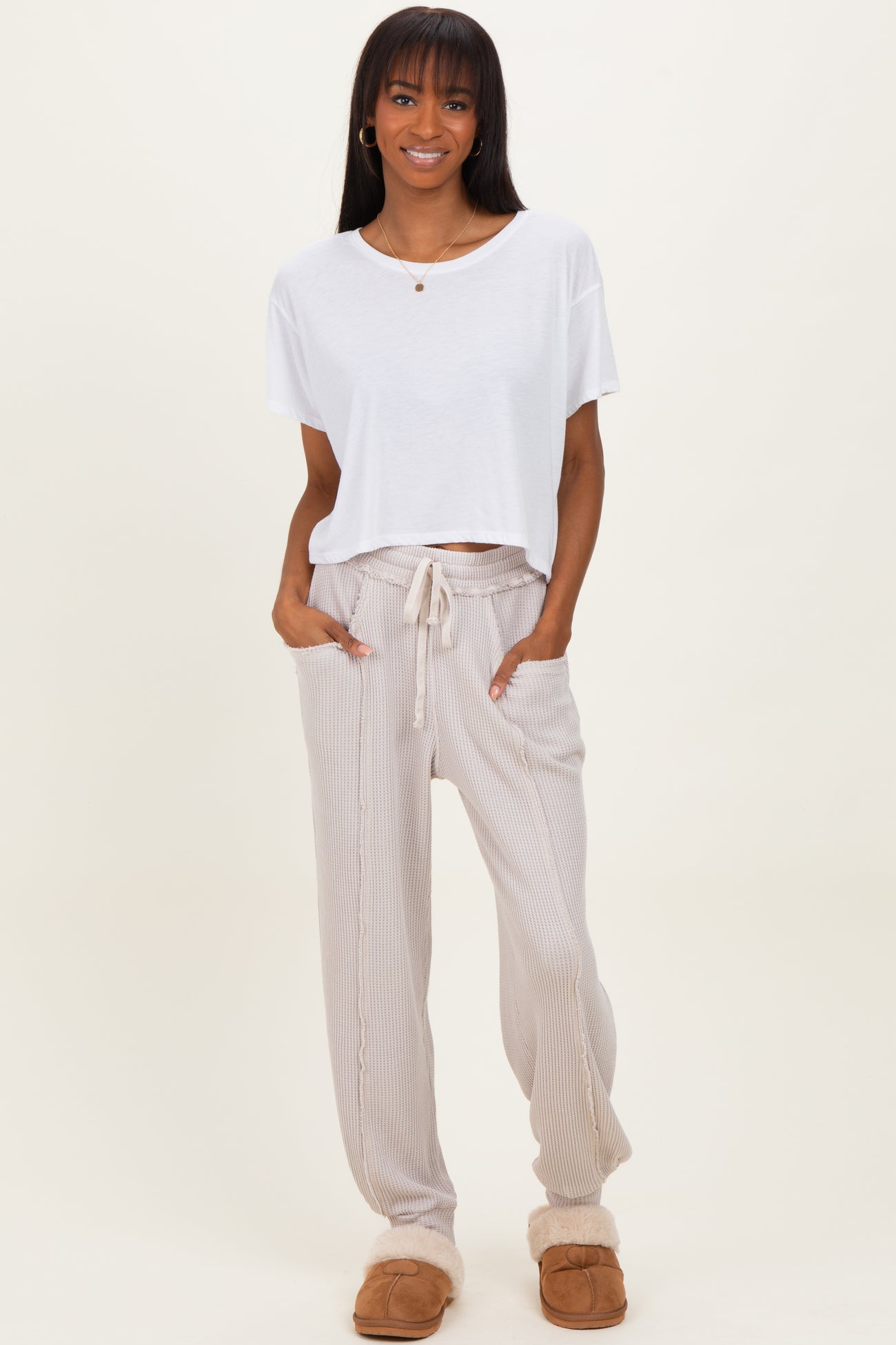 woman wearing a white cropped t-shirt and beige striped drawstring pants, standing in casual slippers
