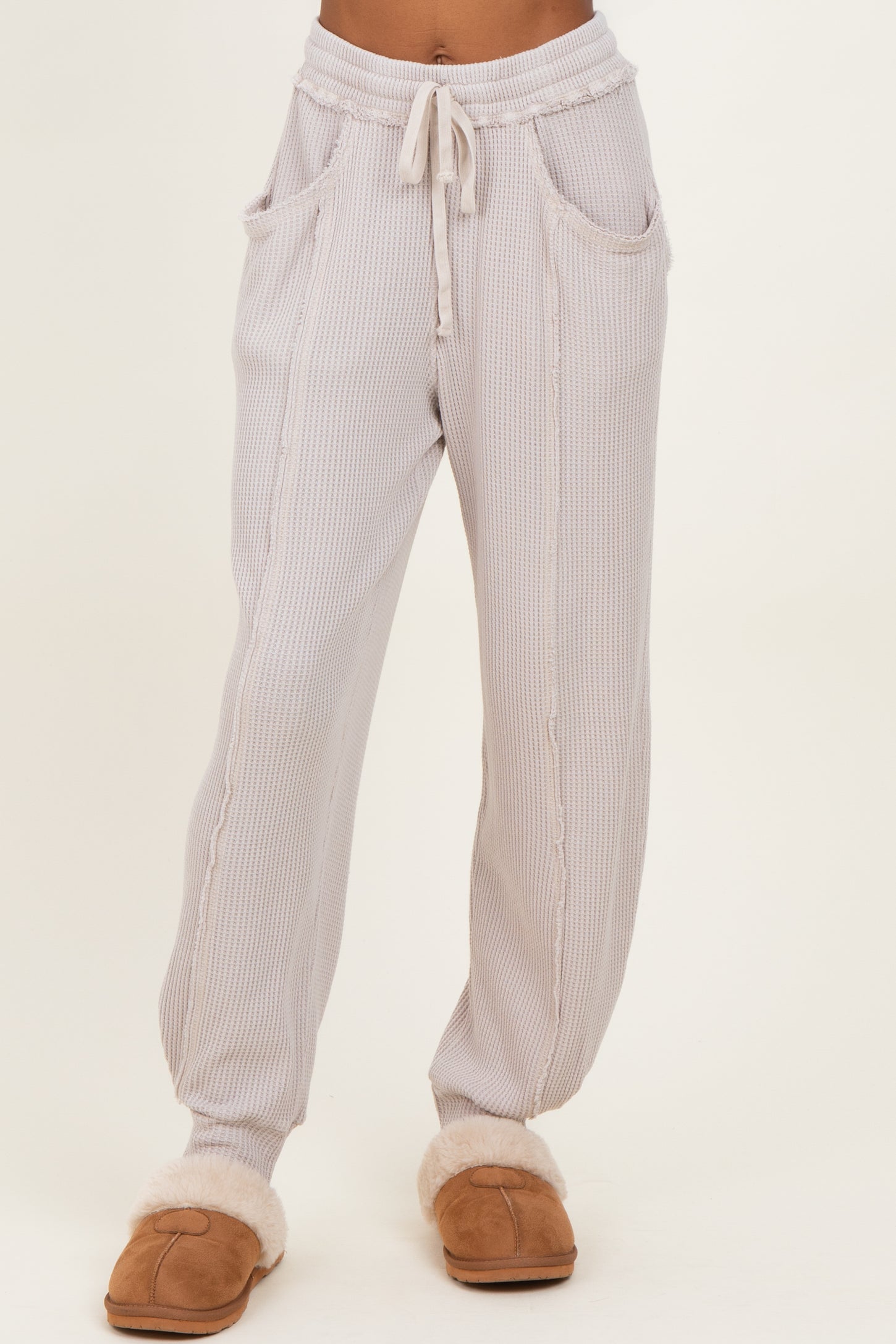 woman wearing light gray ribbed loungewear pants with pockets and drawstring waist, styled with cozy slippers