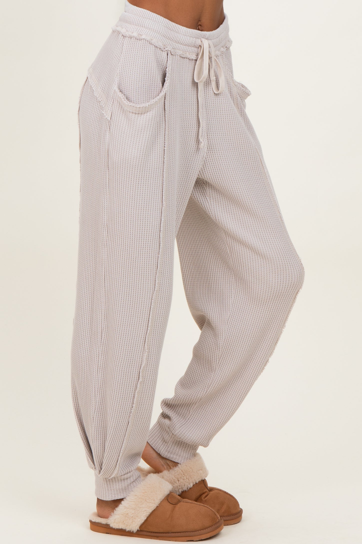 woman wearing light gray striped lounge pants with pockets and a drawstring waist, styled with cozy slippers