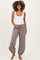 woman wearing a white tank top and gray maternity jogger pants, gently holding her baby bump