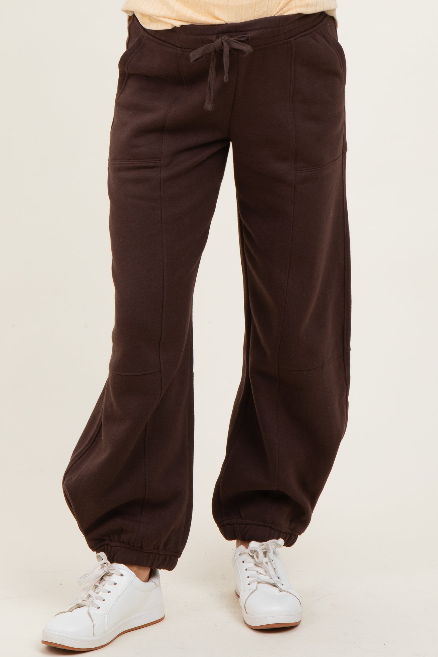 woman wearing brown maternity jogger pants with drawstring and elasticized cuffs, styled with white sneakers