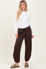 woman wearing a white long sleeve top and brown jogger pants with a drawstring, standing in a relaxed pose