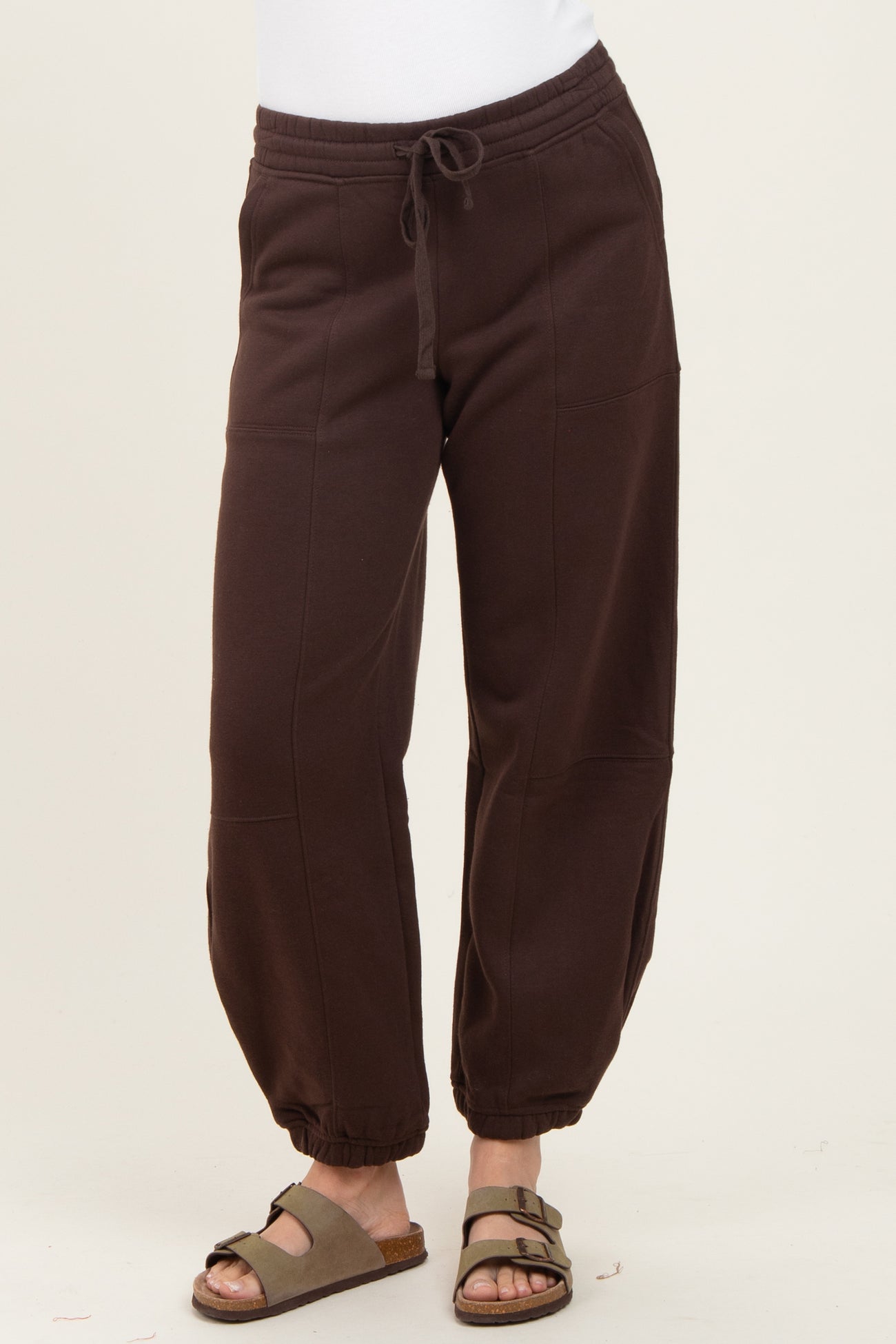 woman wearing dark brown jogger pants with an elastic waistband and gathered cuffs, paired with slide sandals