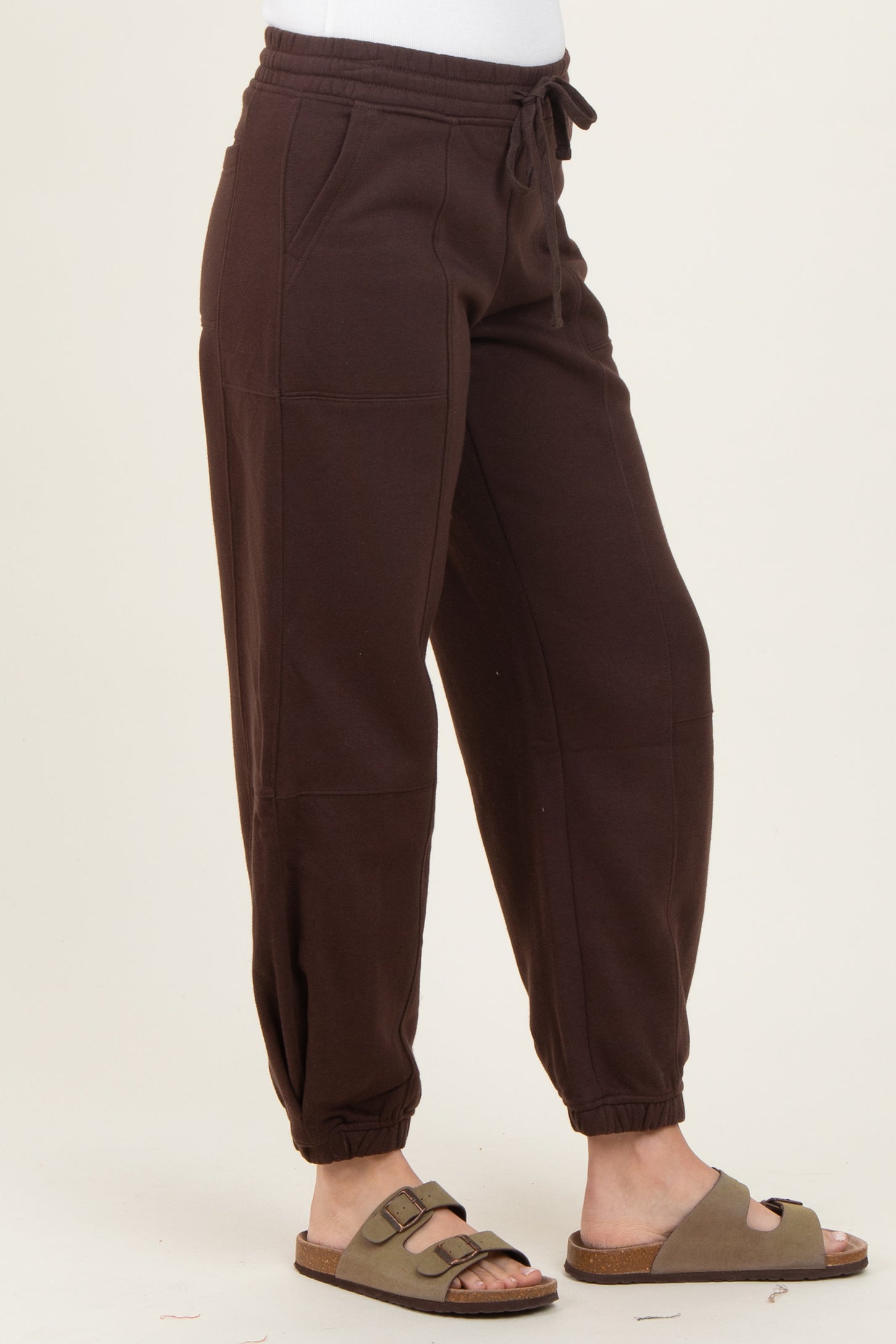 woman wearing brown jogger pants with elastic cuffs and a drawstring waist, styled with tan slip-on sandals