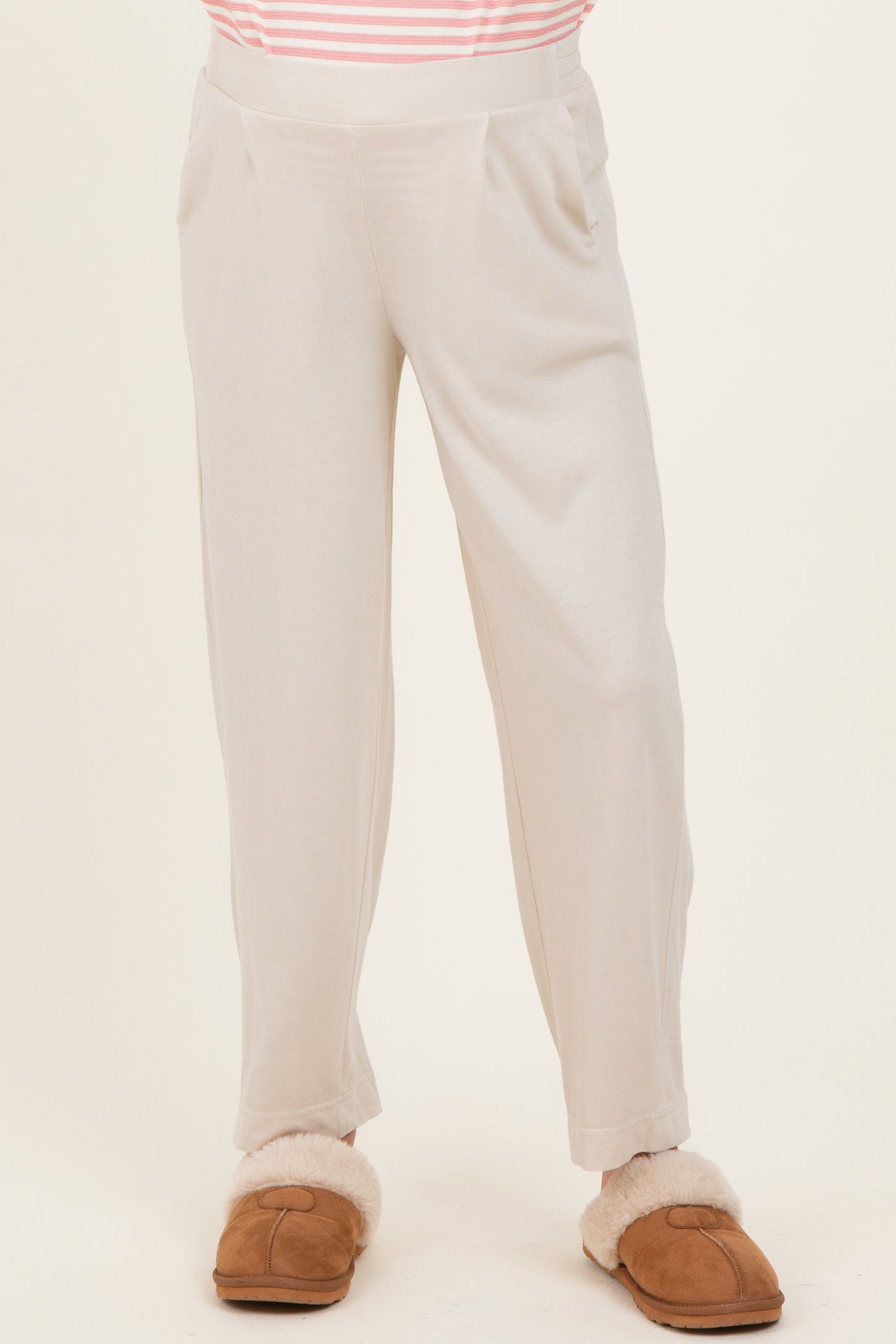 woman wearing light beige maternity pants with a relaxed fit and side pockets, paired with brown fuzzy slippers