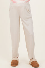 woman wearing light beige maternity pants with a relaxed fit and side pockets, paired with brown fuzzy slippers