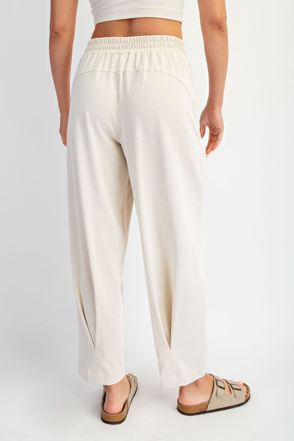 woman wearing relaxed fit cream-colored pants with a drawstring waist and side pockets, standing with back to camera