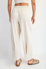 woman wearing relaxed fit cream-colored pants with a drawstring waist and side pockets, standing with back to camera