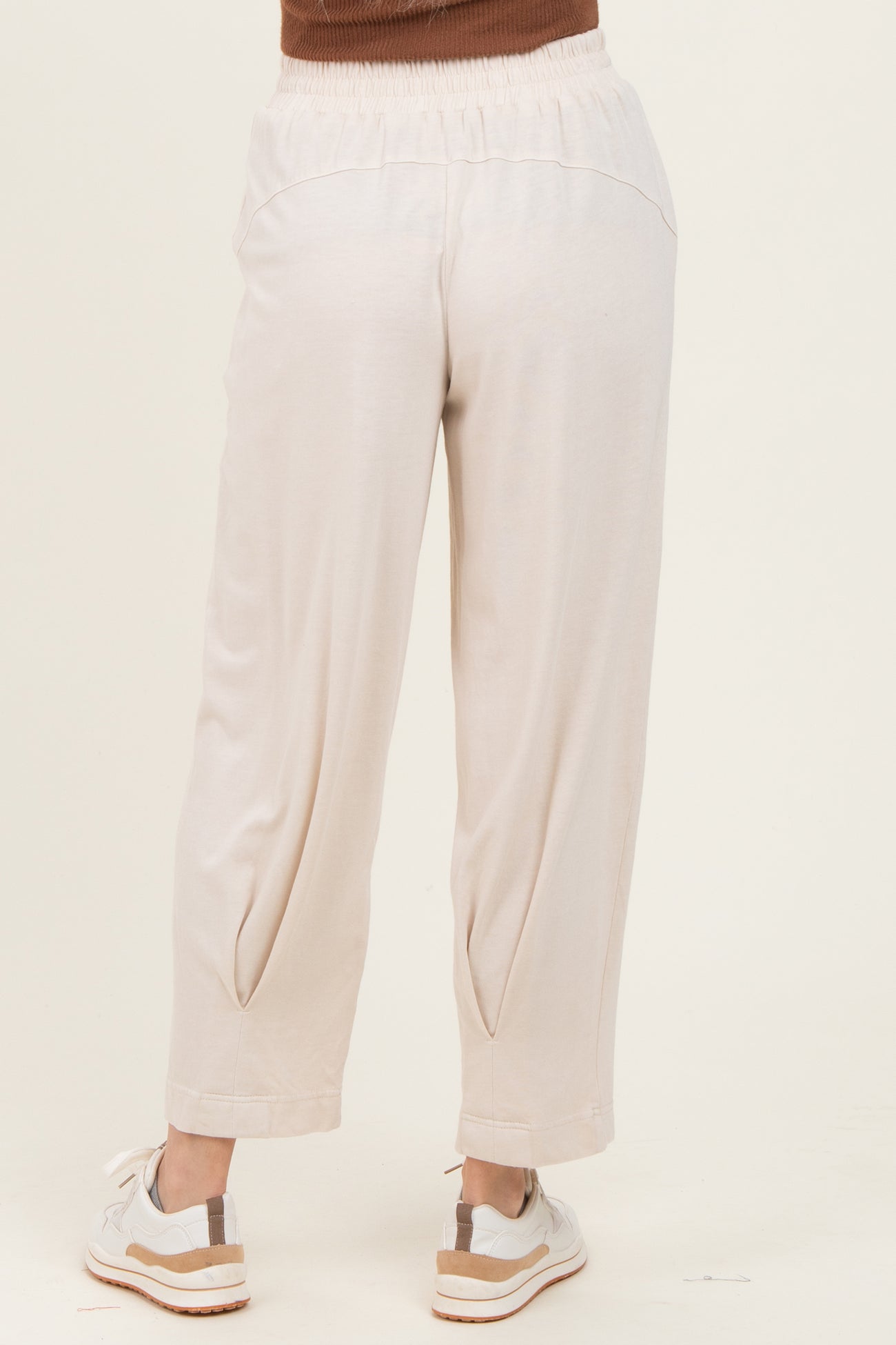 woman wearing light beige loose-fitting pants with an elastic waistband and tapered legs, seen from the back