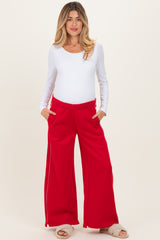 woman wearing a white long sleeve maternity top and red wide-leg maternity pants with pockets, showing her baby bump
