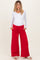 woman wearing a white long sleeve maternity top and red wide-leg maternity pants with pockets, showing her baby bump