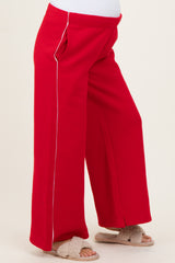 maternity wear red wide-leg pants with white piping details, model wearing them and showing a baby bump