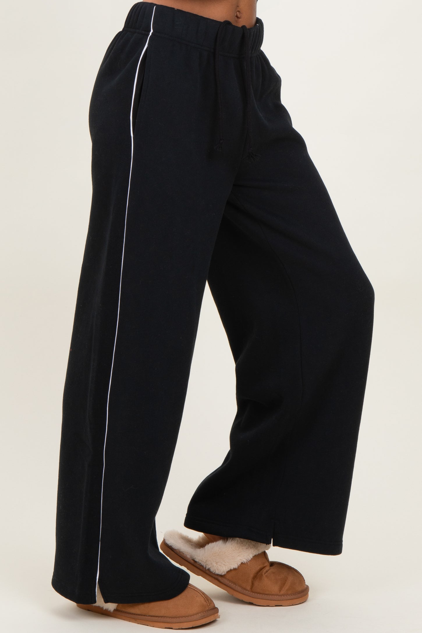 woman wearing black wide-leg sweatpants with white side stripe and tan slippers
