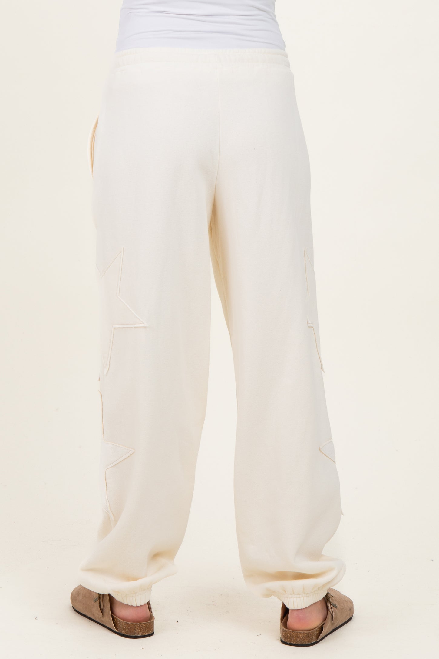 woman wearing cream maternity jogger pants with star details on the sides, showing the back view