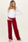woman wearing a white long sleeve maternity top and red ribbed maternity pants, holding her baby bump