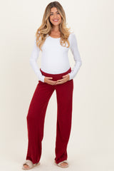 woman wearing a white long sleeve maternity top and red wide-leg maternity pants, holding her baby bump