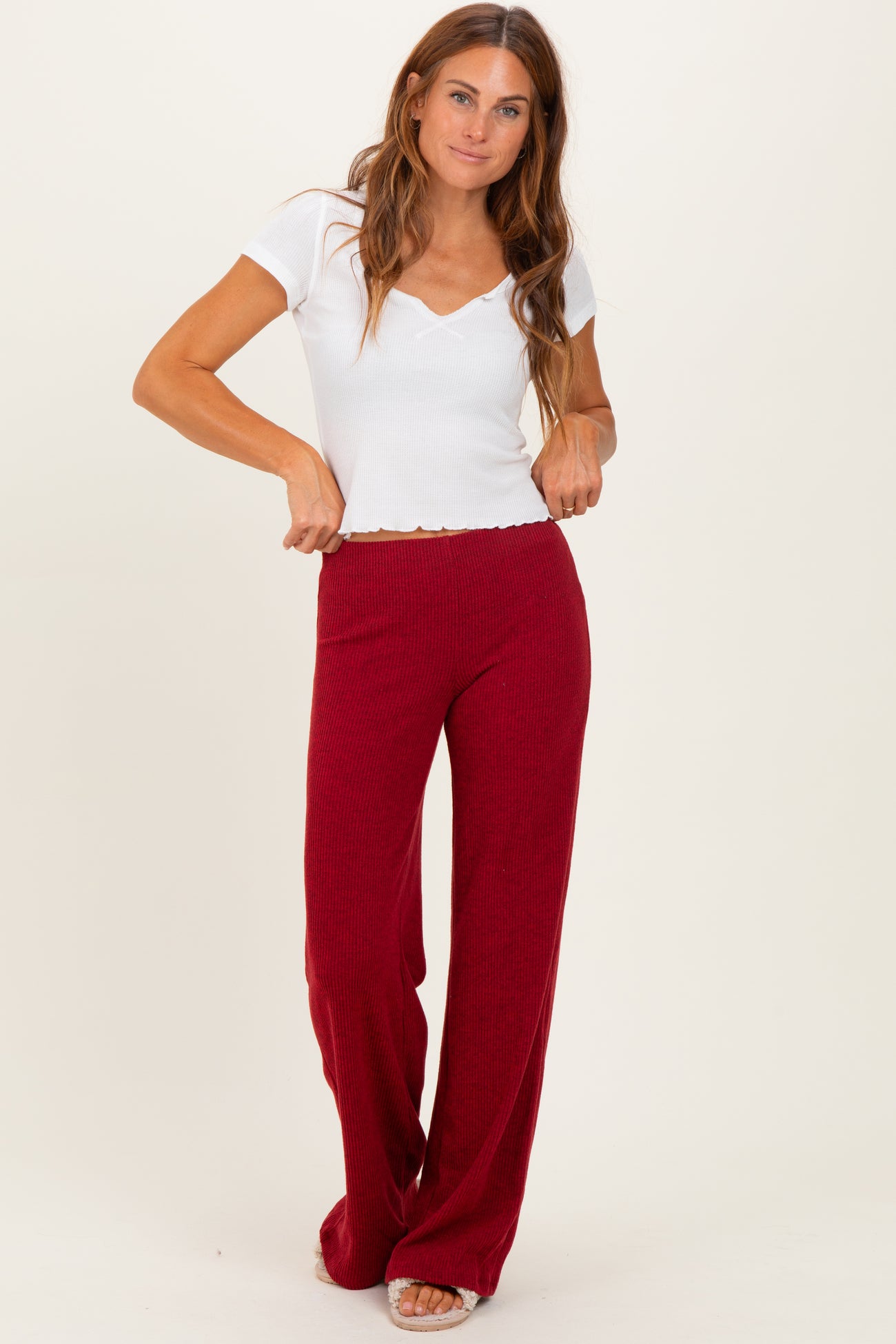 woman wearing a white short sleeve v-neck top and burgundy wide-leg pants, standing with hands on waistband