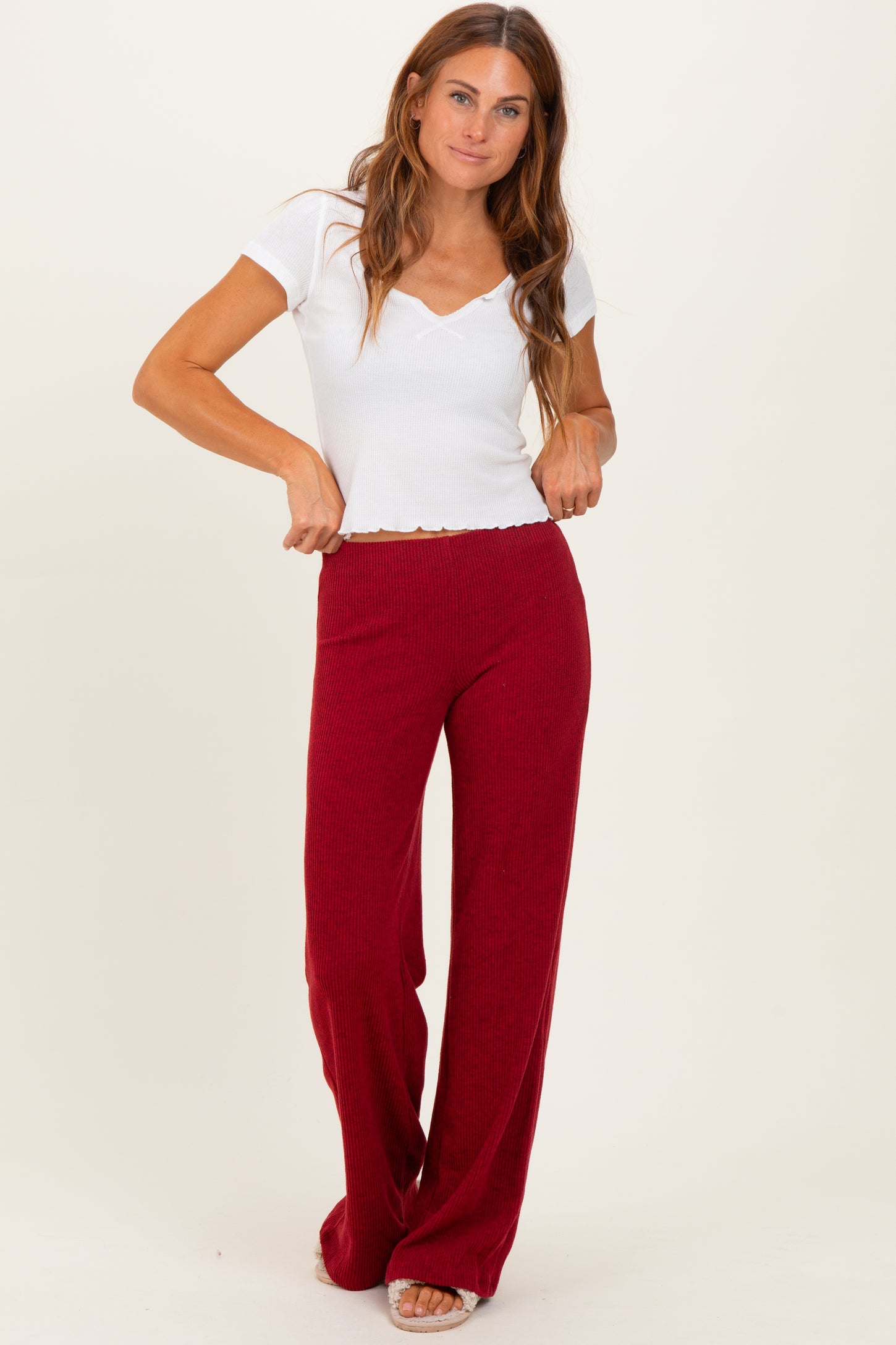 woman wearing a white short sleeve v-neck top and burgundy wide-leg pants, standing with hands on waistband
