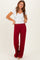 woman wearing a white short sleeve v-neck top and burgundy wide-leg pants, standing with hands on waistband