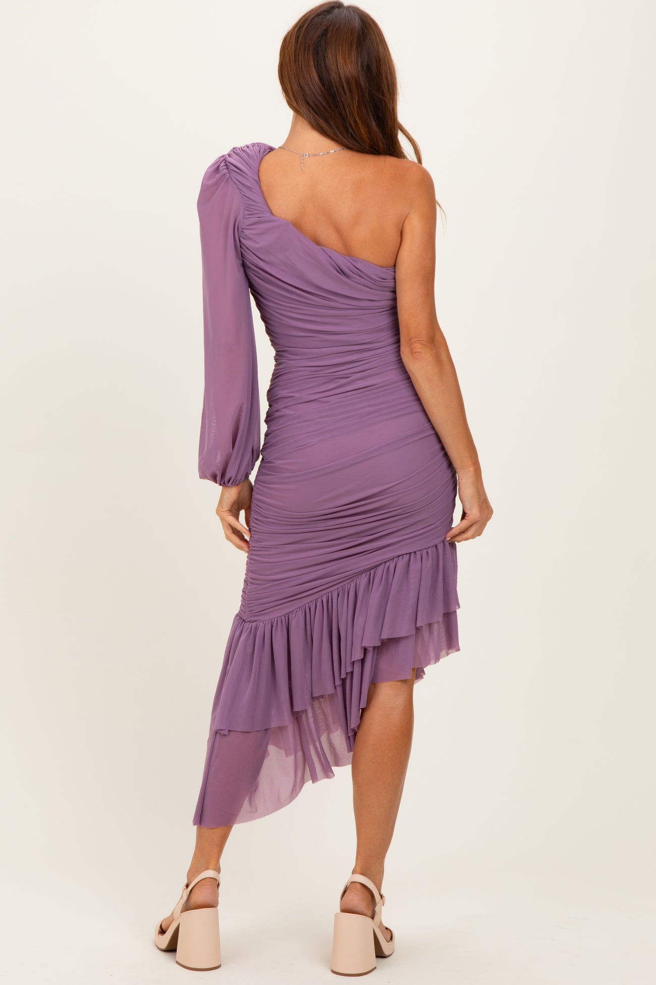 woman wearing a purple one-shoulder ruched dress with a ruffled hem and long sleeve detail