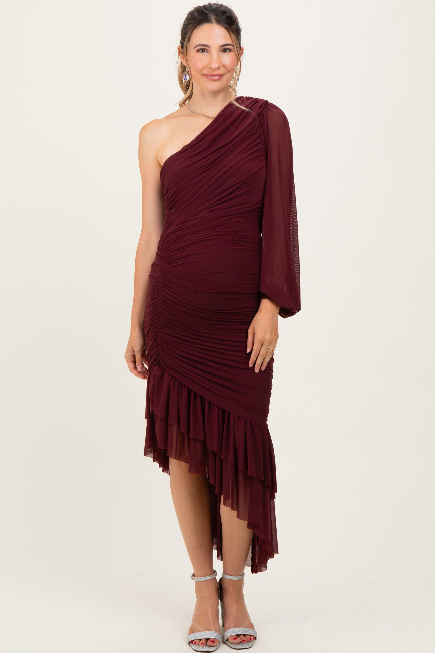 woman wearing a burgundy one-shoulder maternity dress with ruched detailing and a ruffled hem, showcasing a baby bump