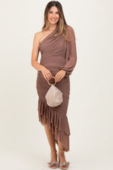 woman wearing a brown one-shoulder maternity dress with ruching and a ruffled hem, holding a small bag
