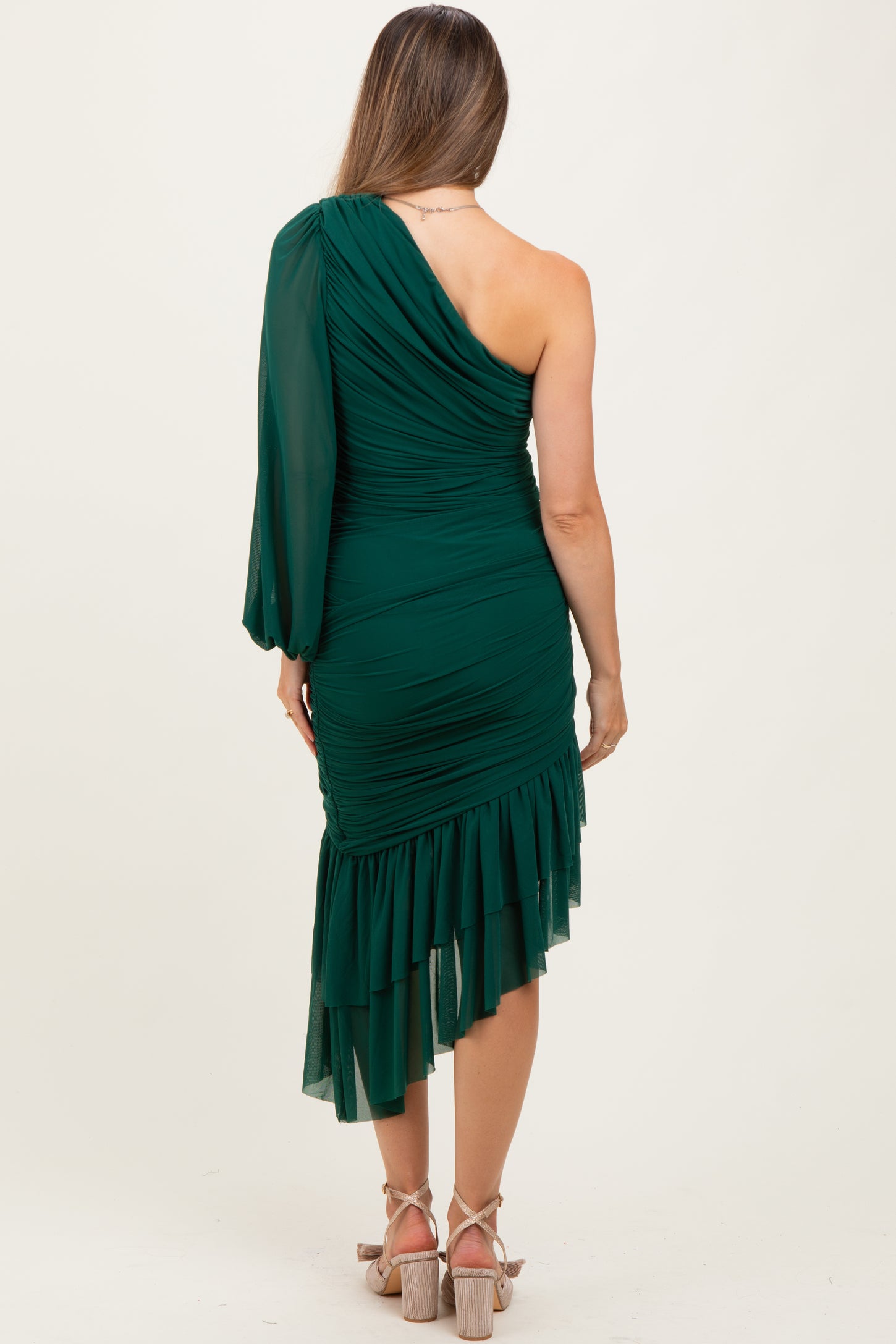 woman wearing a green one-shoulder maternity dress with ruching and a ruffled hem, seen from the back