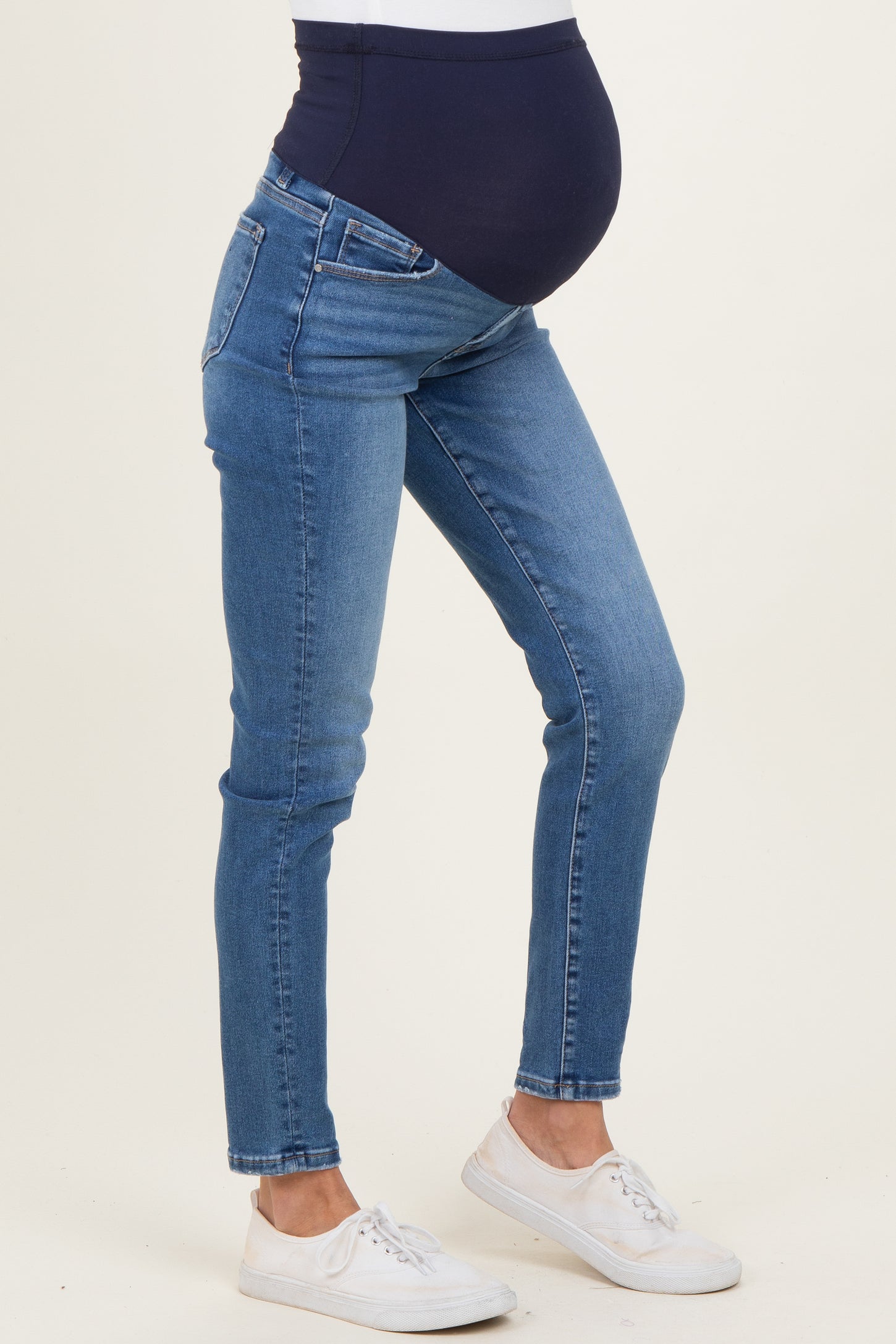 woman wearing a pair of blue maternity skinny jeans with a dark blue over-the-bump waistband and a visible baby bump
