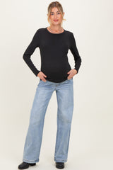 woman wearing a black long sleeve maternity top and light blue wide-leg jeans, showcasing her baby bump