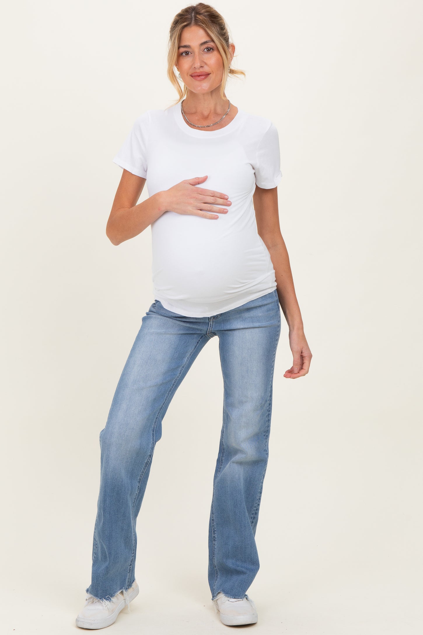 woman wearing a white short sleeve maternity top and light blue jeans, holding her baby bump