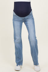 woman wearing a pair of light blue maternity jeans with a navy belly panel and white sneakers, showcasing her baby bump