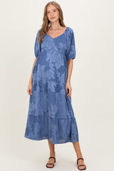 woman wearing a blue floral maternity maxi dress with puff sleeves and a defined waist, showcasing her baby bump