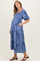 woman wearing a blue floral maternity dress with short puff sleeves and pockets, showing a baby bump