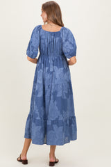woman wearing a navy blue floral maternity maxi dress with puff sleeves and a tiered skirt, showing her baby bump