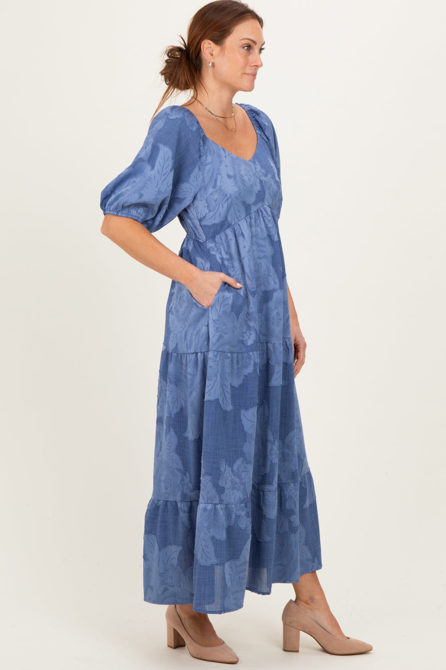 woman wearing a blue floral tiered midi dress with puff sleeves and pockets, paired with nude heel sandals
