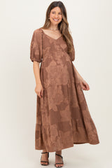 woman wearing a brown floral print maternity maxi dress with short puff sleeves and a tiered skirt, gently cradling her baby bump