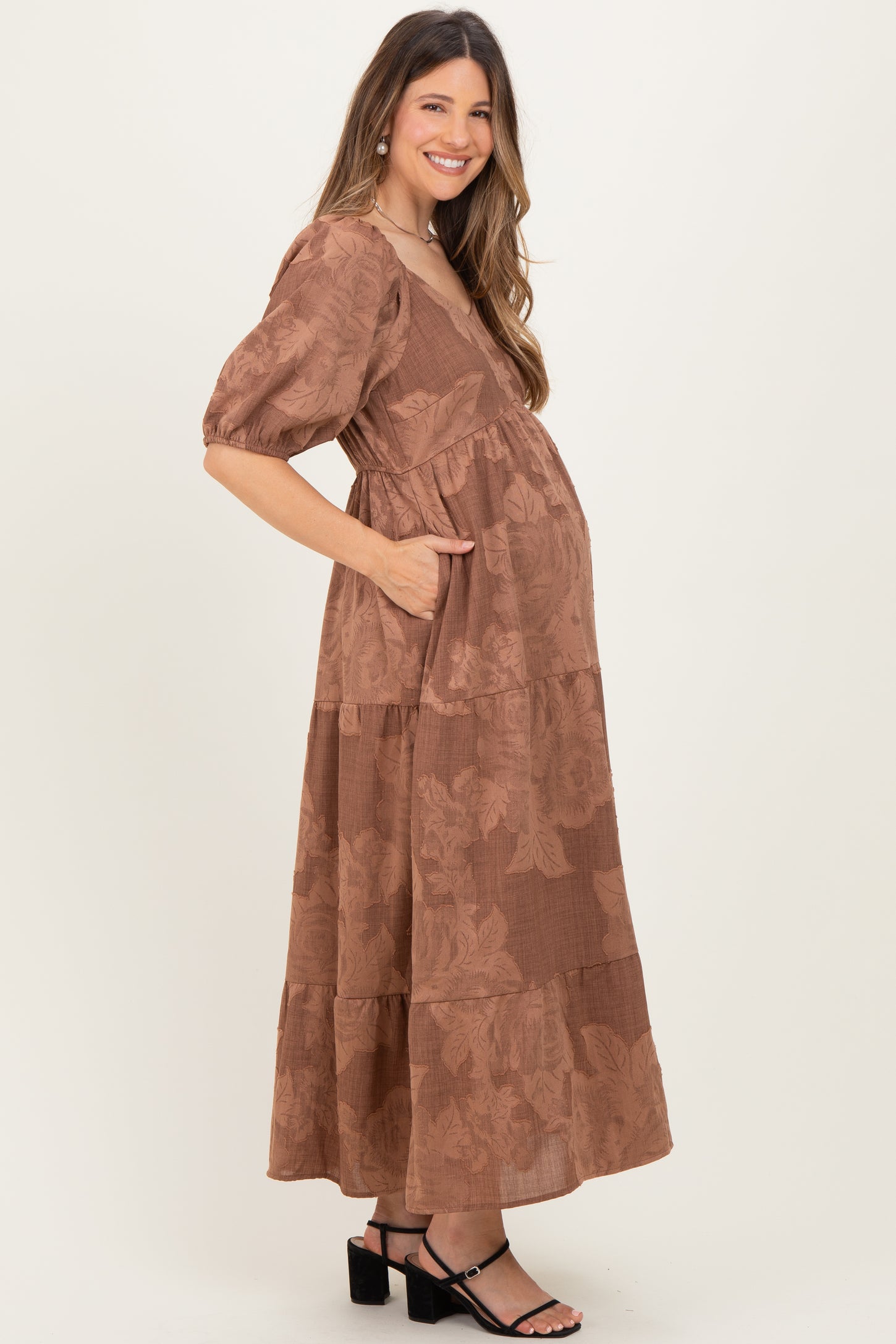 woman wearing a brown floral print maternity maxi dress with pockets and a visible baby bump