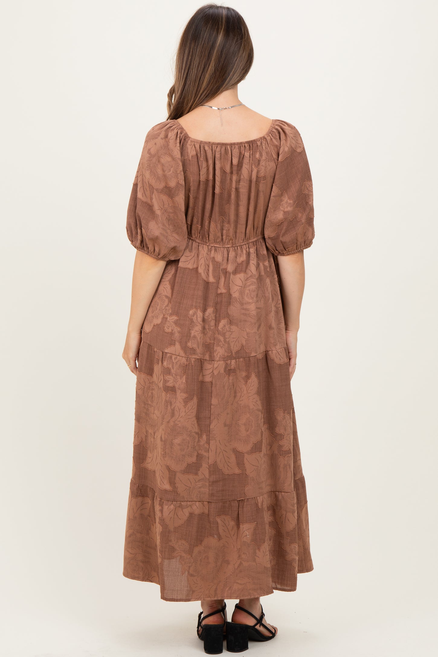 woman wearing a brown floral maternity maxi dress with puff sleeves and a tiered hem, showing a baby bump