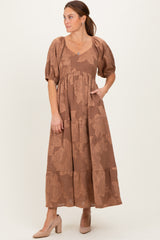 woman wearing a brown floral maxi dress with puff sleeves and a tiered skirt, standing with one hand in the pocket