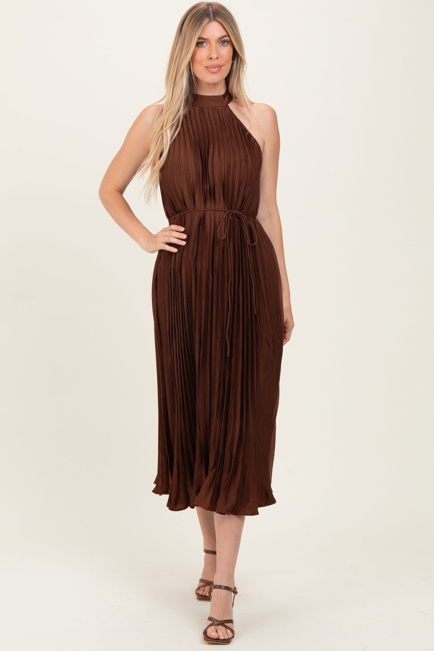 woman wearing a brown pleated midi dress with a halter neckline and a tied waist detail