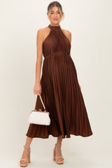 woman wearing a brown pleated maternity dress with a halter neck and a tie at the waist, holding a white handbag